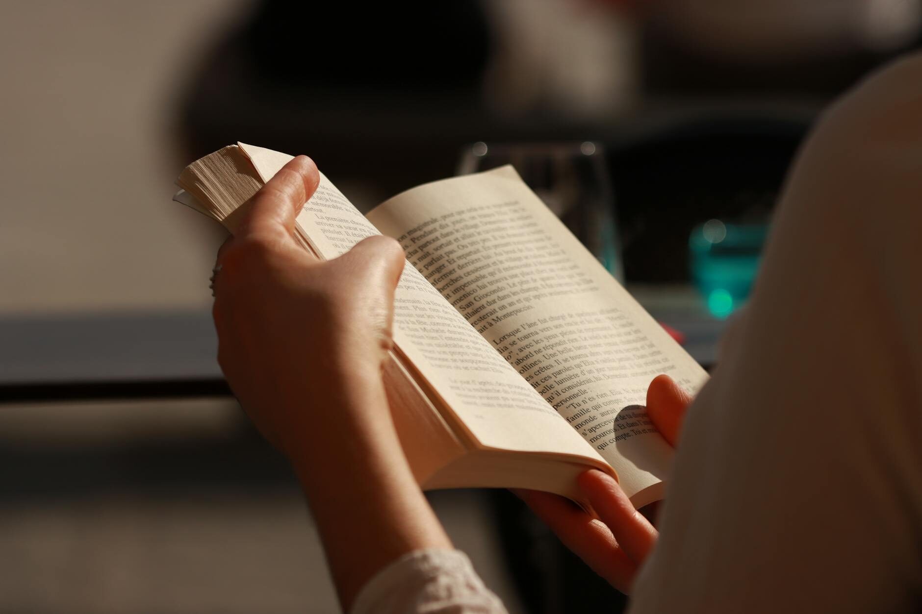 Close-up of hands holding an open paperback book in warm golden afternoon light
