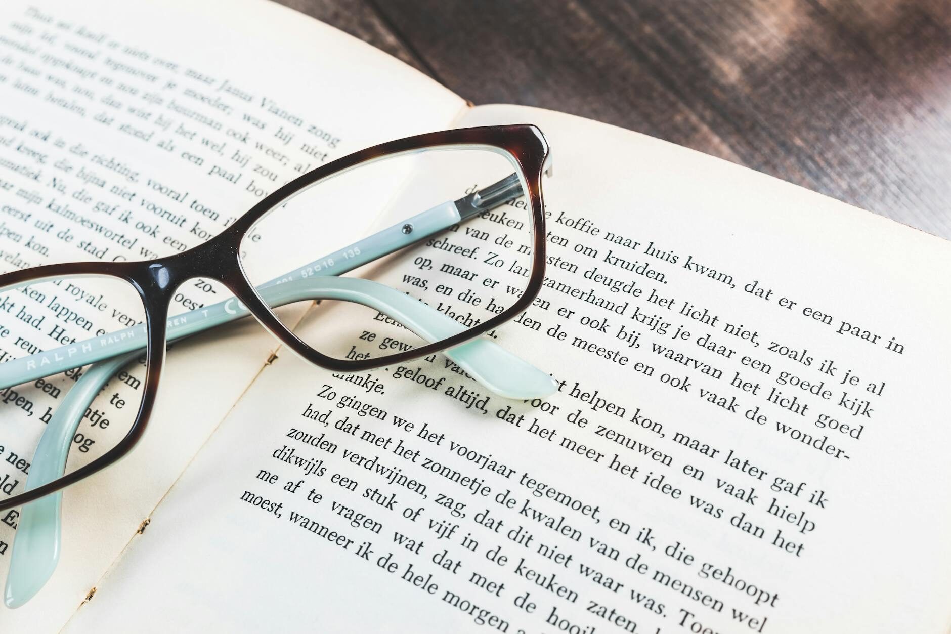 Black-framed eyeglasses resting on open book pages against a clean white background